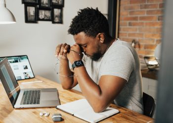 a tired man rubbing his eyes while sitting in front of his laptop